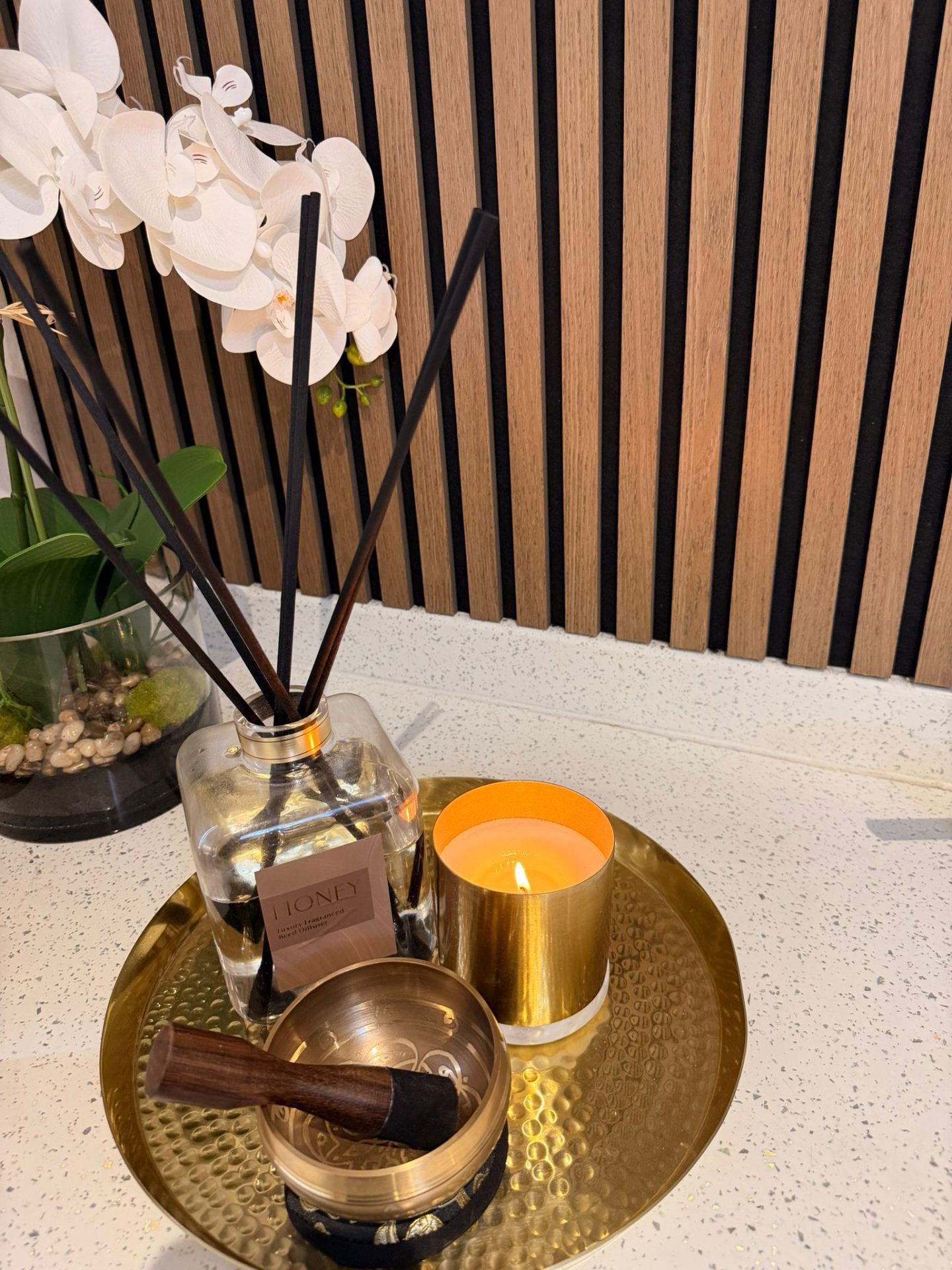 Honey reed diffuser, brass singing bowl and candle on a tray at Opal